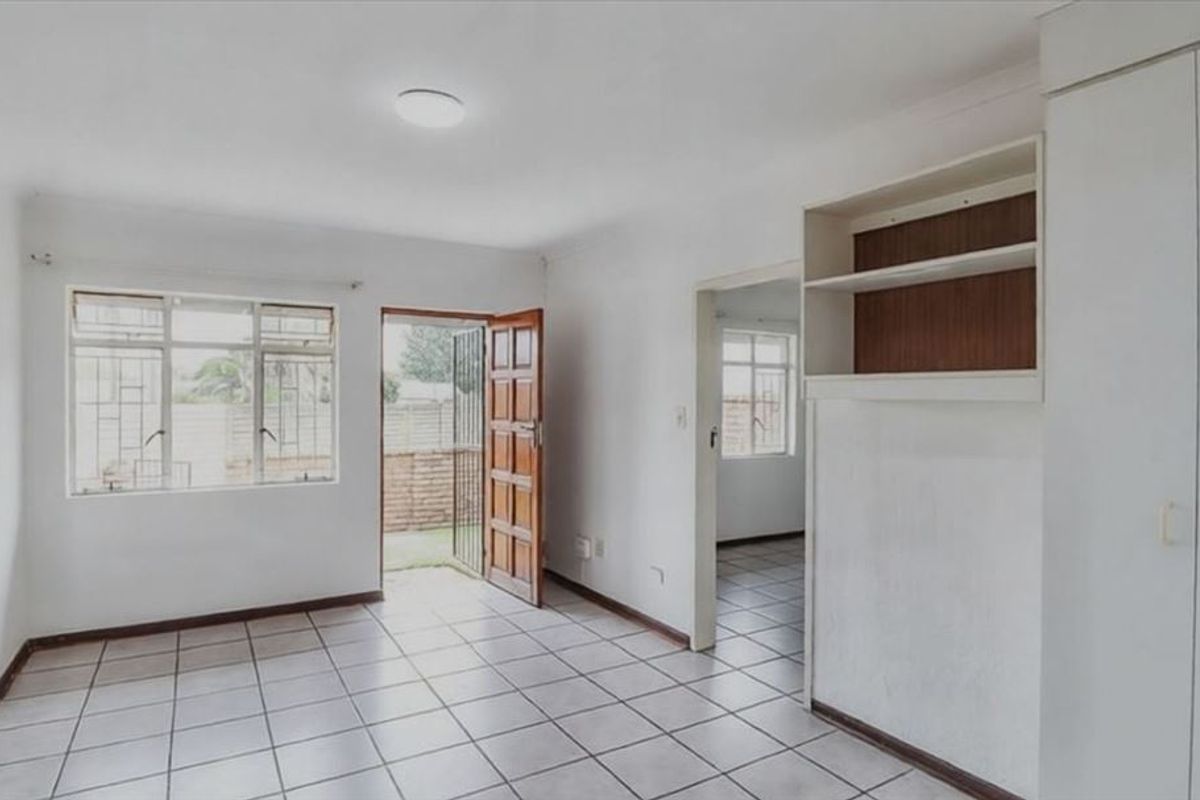 An empty bedroom featuring tiled flooring, built-in cupboards, and direct access to an outdoor area through a security gate.