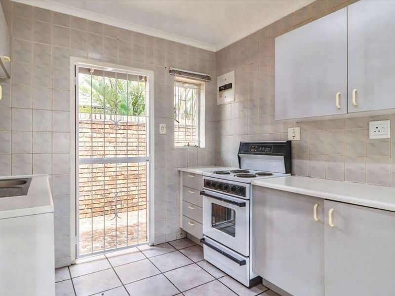 A functional kitchen featuring tiled walls and floors, built-in cabinetry, and a freestanding stove, with direct access to an outdoor area.