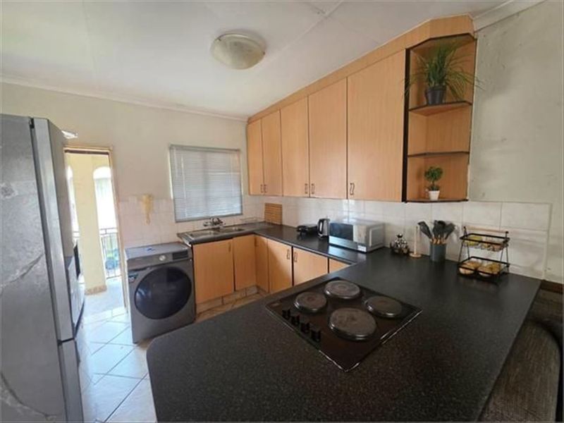 A functional kitchen featuring laminate cabinetry, dark countertops, an integrated electric hob, and tiled flooring, with direct access to an outdoor area.
