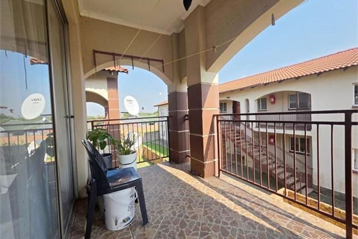 A covered balcony featuring tiled flooring and metal railings, providing an outdoor space with views of the surrounding townhouse complex.