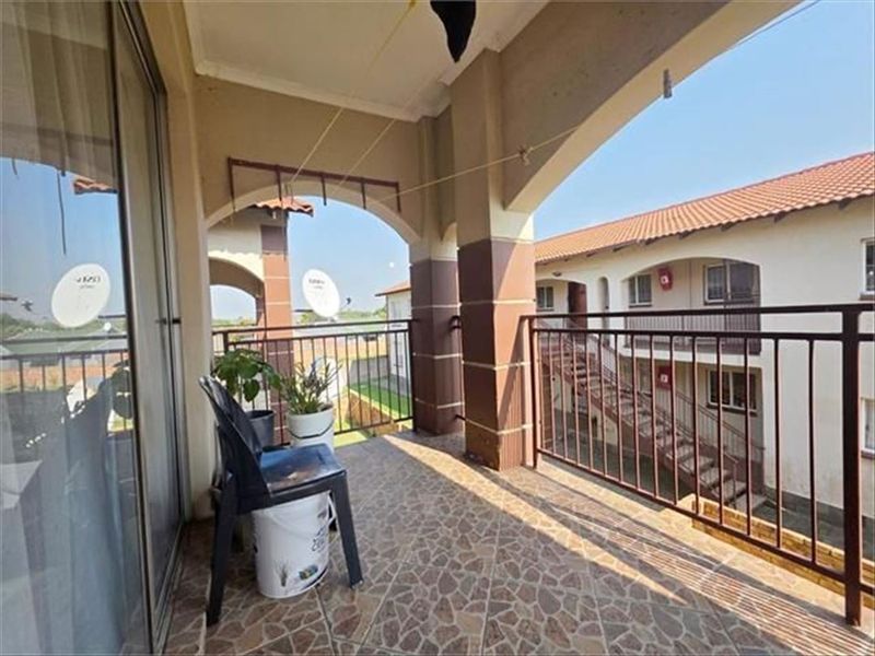 A covered balcony featuring tiled flooring and metal railings, providing an outdoor space with views of the surrounding townhouse complex.