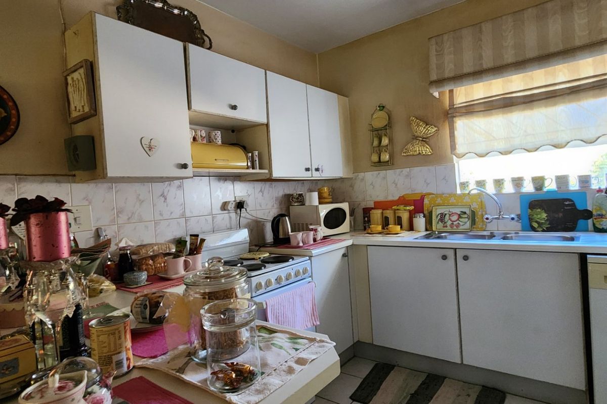 A compact kitchen featuring white cabinetry, tiled backsplash, a stainless steel sink, and a built-in washing machine, offering a functional layout with dated finishes.