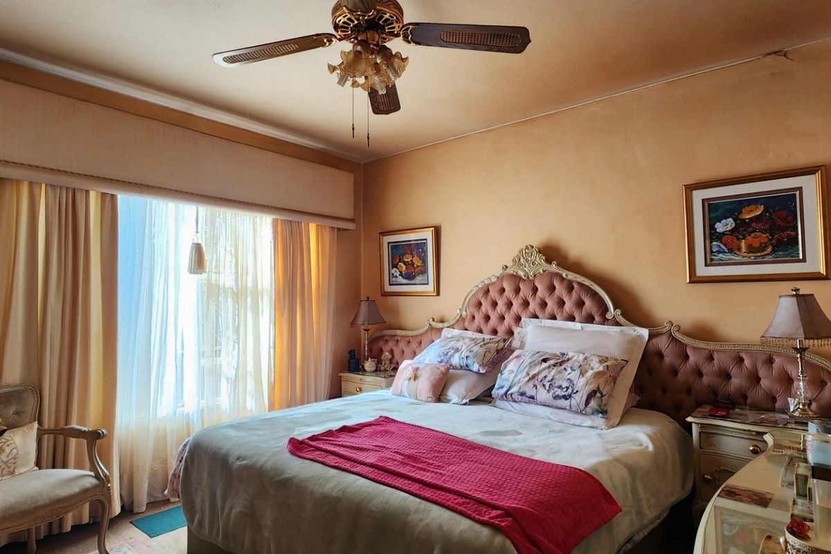 A bedroom featuring a ceiling fan, decorative coving, and a window pelmet. The room shows signs of wear including visible ceiling cracks.
