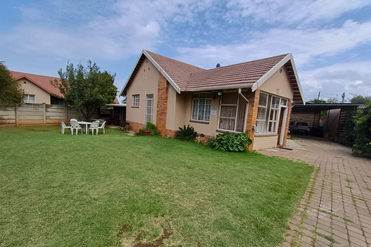 Rear view of a single-story brick house featuring a tiled roof, solar geyser, paved driveway, and a spacious lawn area.