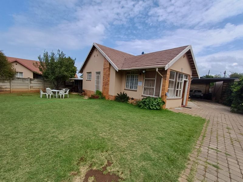 Rear view of a single-story brick house featuring a tiled roof, solar geyser, paved driveway, and a spacious lawn area.