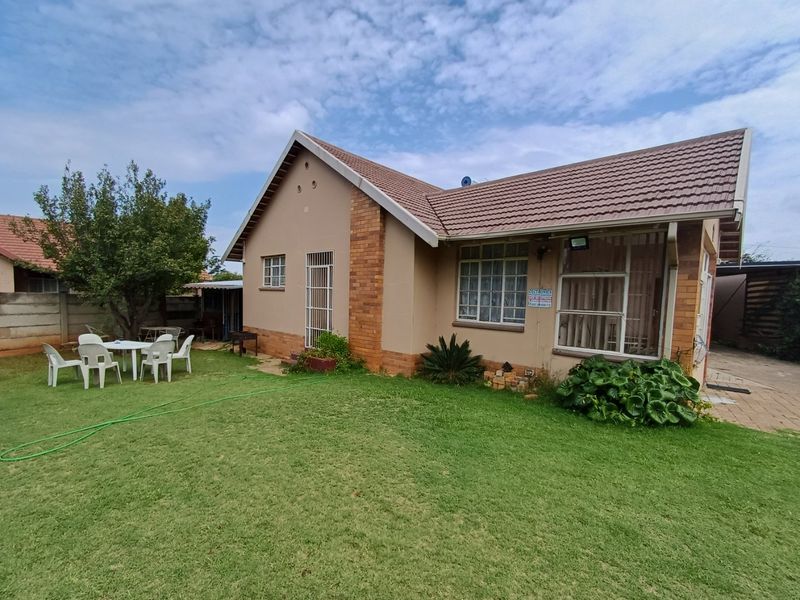 Rear view of a single-story house featuring a tiled roof, brick accents, security bars on windows, and a well-maintained lawn area.