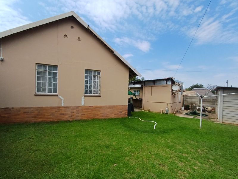 Rear view of the property showing the exterior wall with brick plinth, steel-framed windows, and a spacious grass lawn area.