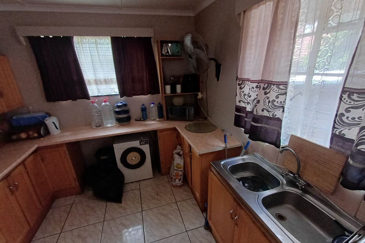 A functional kitchen featuring wooden cabinetry, laminate countertops, a double bowl stainless steel sink, and tiled flooring.