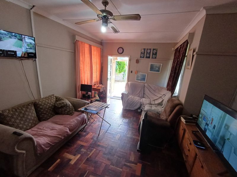 A living room featuring classic parquet flooring, a ceiling fan, and direct access to the exterior through a doorway.