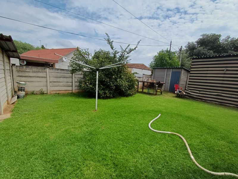 A private backyard featuring a well-maintained lawn, a precast concrete boundary wall, and a functional storage shed.