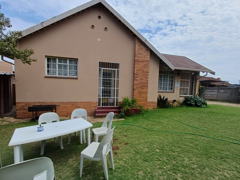 Rear view of the house featuring a brick and plaster facade, tiled roof, security gate, and a spacious lawn area.