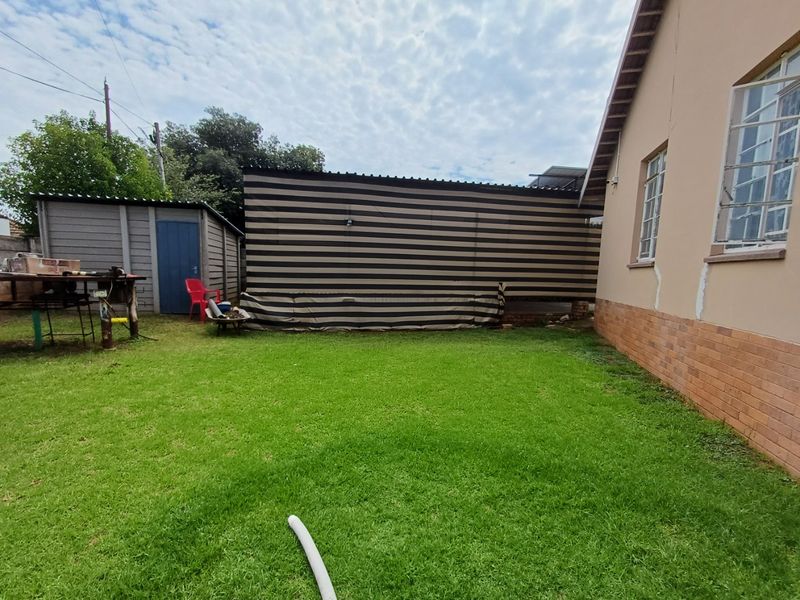 Rear garden area featuring a lawn, a precast concrete shed, and a view of the house exterior with visible wall cracks.