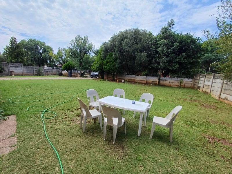 A spacious, well-maintained backyard garden featuring a large lawn area enclosed by precast concrete boundary walls.