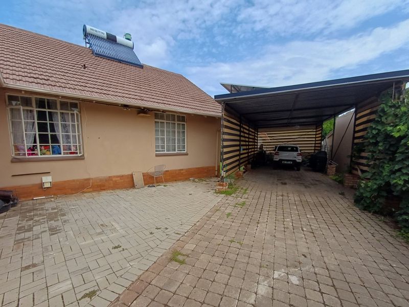 Front exterior view of the house featuring a paved driveway, a covered carport, and a roof-mounted solar water heating system.