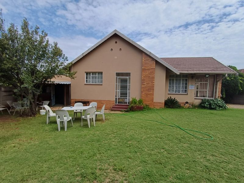Rear view of a single-story house featuring a tiled roof, brick accents, and a spacious garden area with a covered patio.