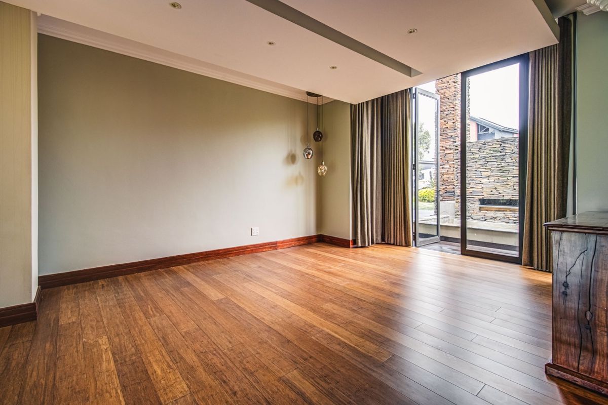 Spacious living area featuring warm timber flooring, recessed ceiling lighting, and large sliding glass doors opening to an outdoor stone-walled patio.