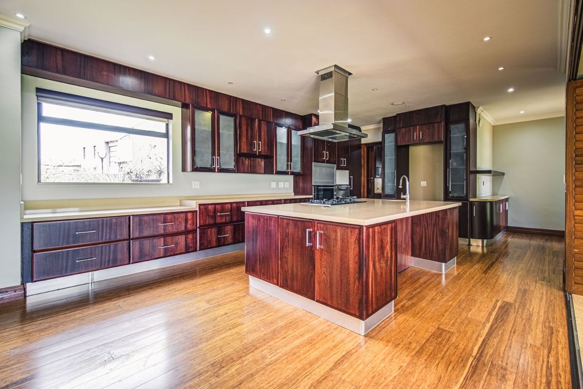 Spacious kitchen featuring dark wood cabinetry, stone countertops, a central island with a built-in hob, and high-quality hardwood flooring.