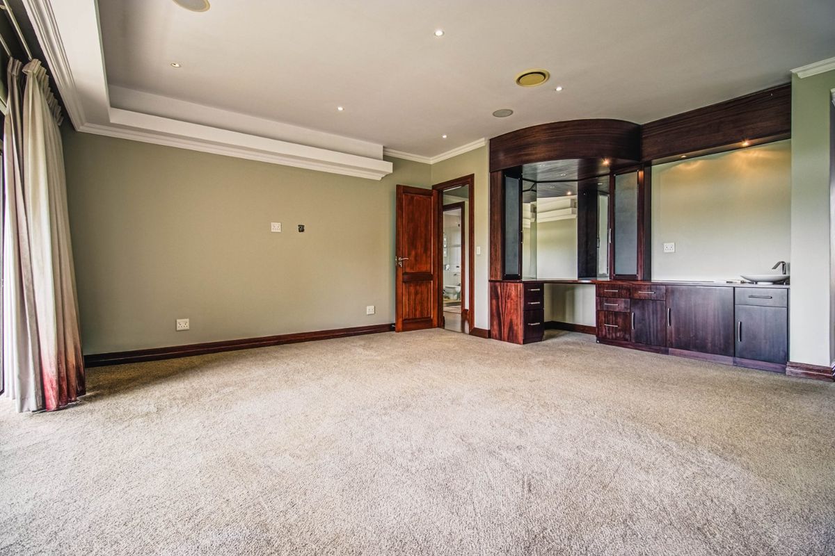 Spacious bedroom featuring neutral walls, plush carpeting, recessed lighting, and a custom built-in timber vanity unit with integrated sink.