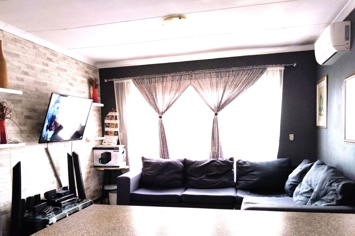 A living room featuring a stone-effect accent wall, split-system air conditioning, and large window with curtain treatments.