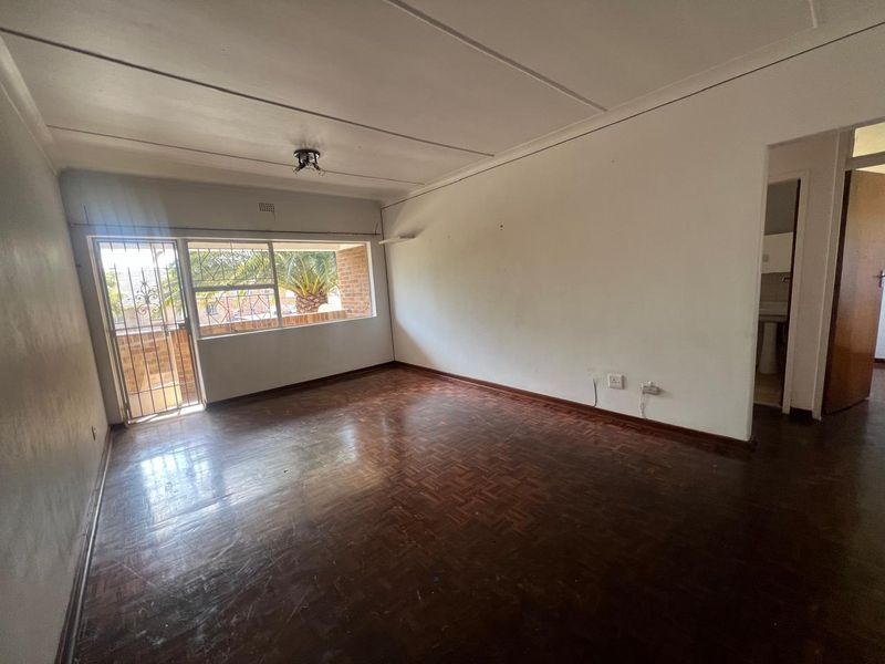 Spacious, empty living room featuring original parquet flooring, large windows with security gate, and neutral walls, offering a blank canvas for renovation.