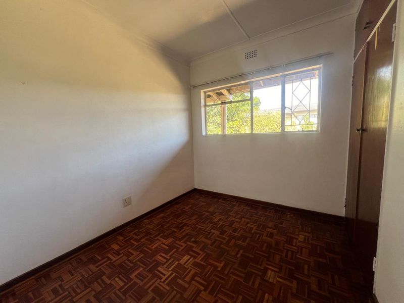 An empty bedroom featuring traditional parquet flooring, a built-in cupboard, and a window fitted with security burglar bars.