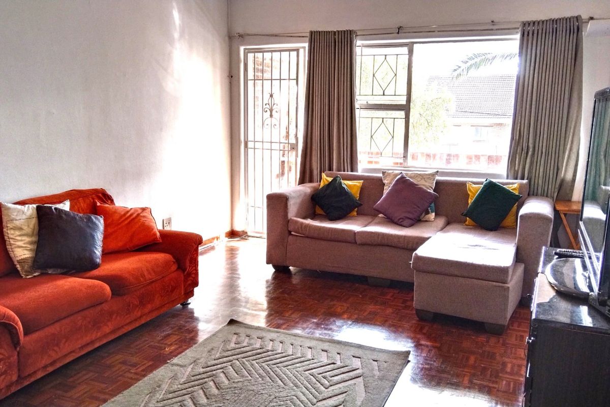 A living room featuring traditional parquet flooring, a large window for natural light, and a security gate leading to the exterior.