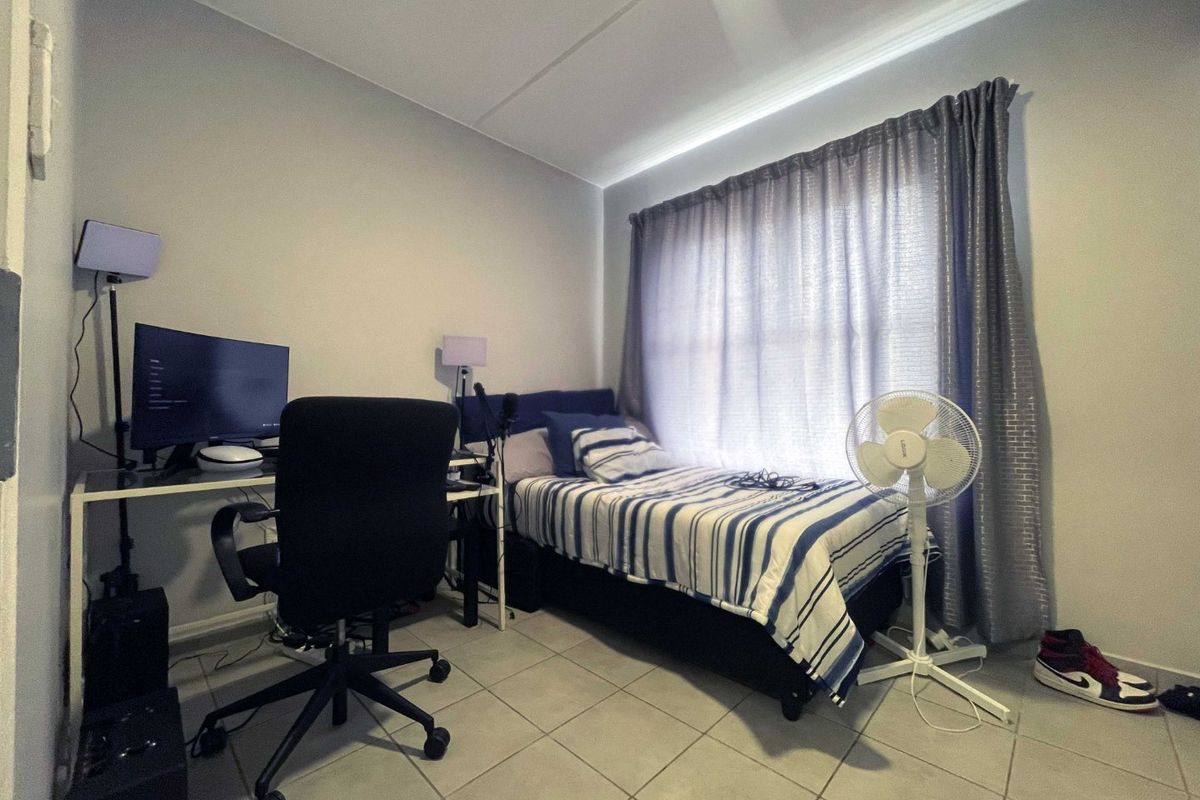 A functional bedroom featuring tiled flooring and window treatments, suitable for use as a sleeping area or home office space.