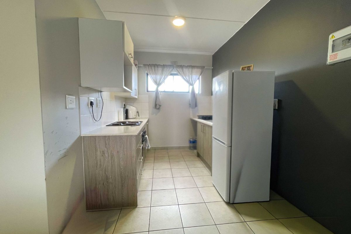 A functional galley-style kitchen featuring tiled flooring, built-in cabinetry, a hob, and a tiled backsplash, providing a practical workspace.