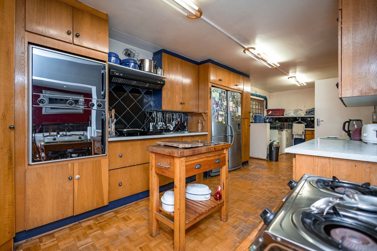 A dated kitchen featuring wooden cabinetry, built-in oven, extractor fan, and parquet flooring, offering significant potential for a modern renovation.