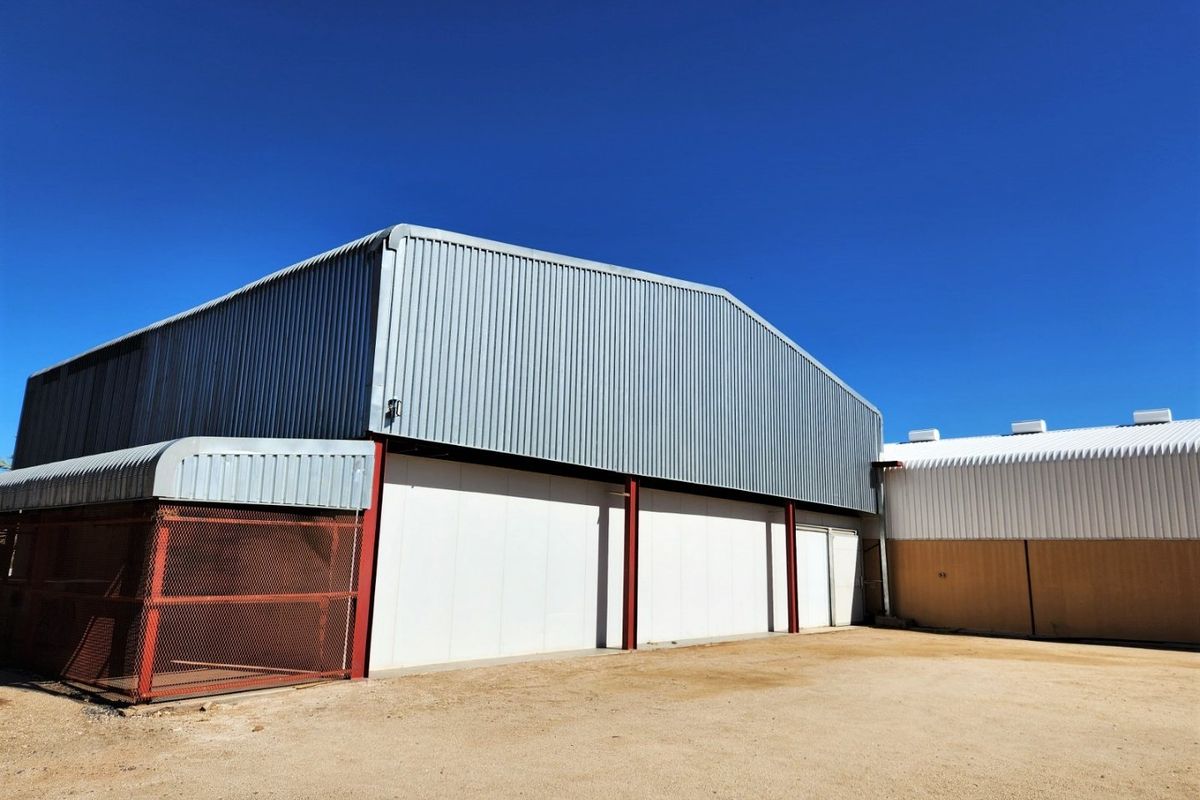 Exterior view of a large industrial-style farm shed featuring corrugated metal cladding, steel structural supports, and expansive sliding access doors.
