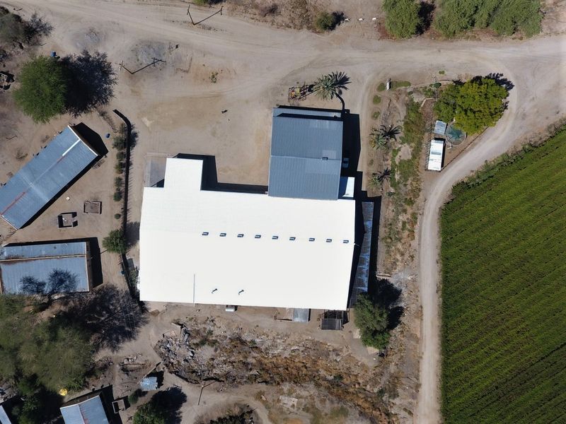 Aerial view of a farm property featuring a large main structure with metal roofing, surrounding outbuildings, gravel access paths, and adjacent agricultural fields.