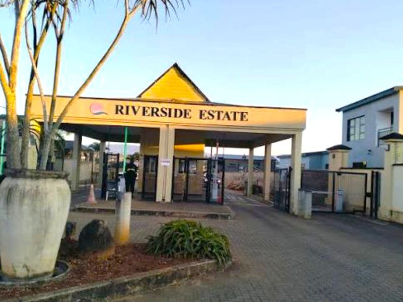 The main entrance and security gatehouse for Riverside Estate, featuring a paved driveway and controlled access point.