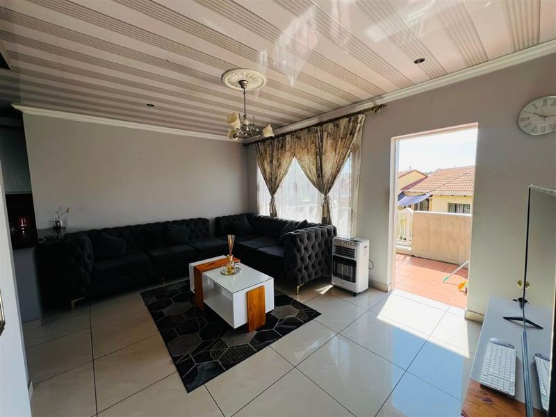 A living room featuring tiled flooring, a decorative ceiling rose, and direct access to an outdoor balcony area.
