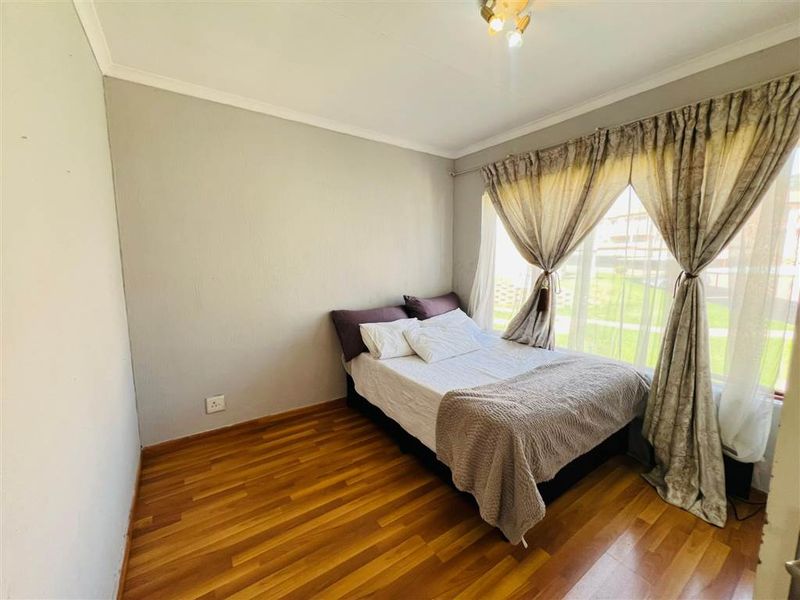 A bedroom featuring laminate flooring and large windows with curtain rails, providing natural light and a view of the exterior grounds.