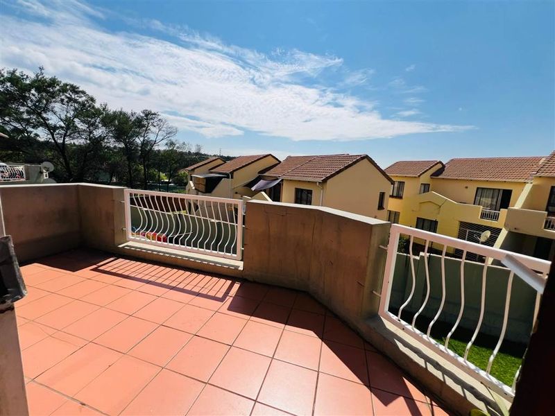 An open-air balcony featuring tiled flooring and a white metal balustrade, offering views of the surrounding residential complex.