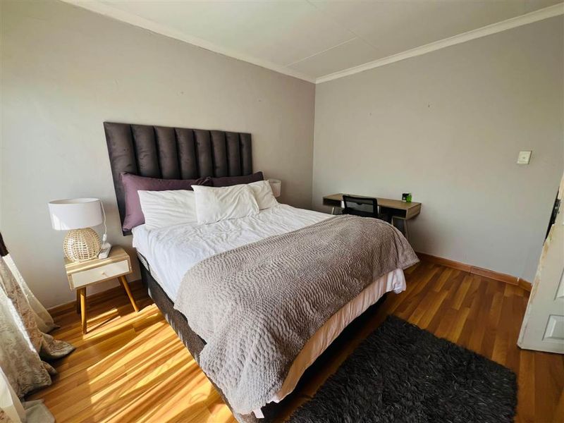 A well-lit bedroom featuring warm-toned laminate flooring and neutral wall finishes, providing a comfortable and functional living space.