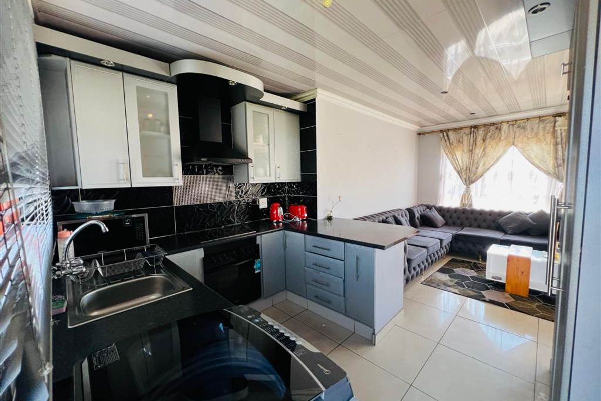 Open-plan kitchen and living area featuring modern cabinetry, integrated appliances, tiled flooring, and a contemporary drop ceiling design.