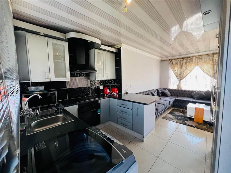 Open-plan kitchen and living area featuring modern cabinetry, integrated appliances, tiled flooring, and a contemporary drop ceiling design.