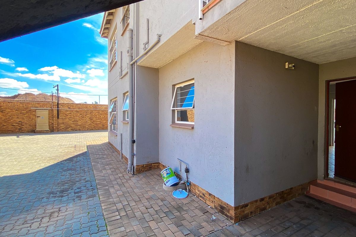 Rear exterior view of the apartment building featuring a paved courtyard area, brick boundary wall, and functional louvre windows.