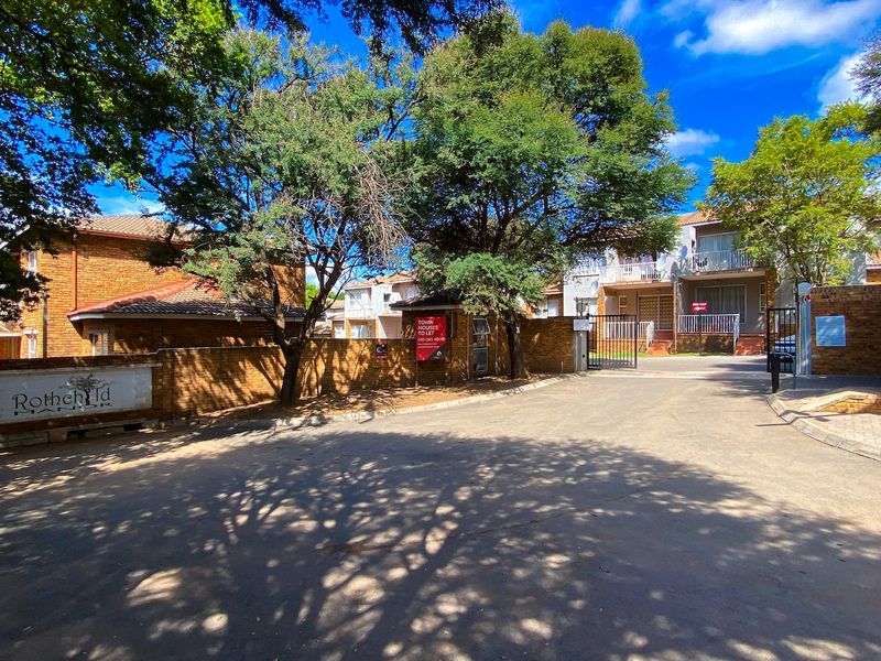 Street view of the entrance to Rothchild Manor, featuring a brick boundary wall, secure gated access, and paved driveway.