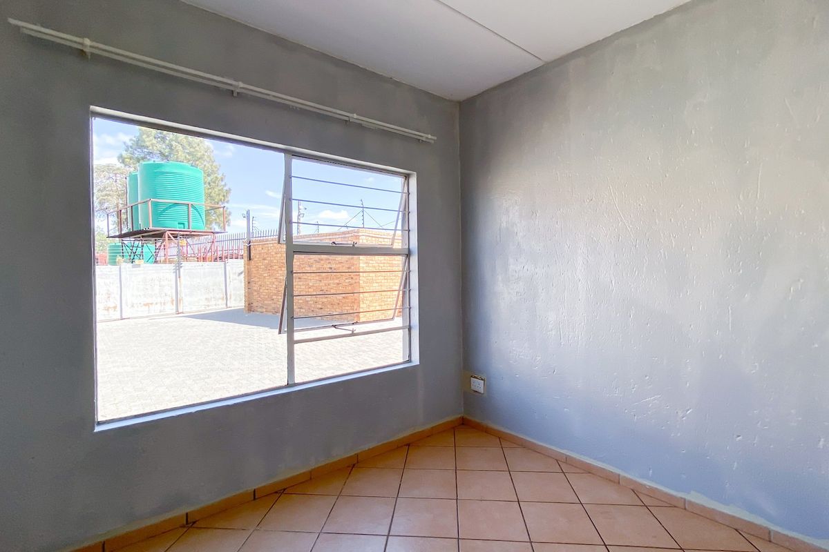 An empty bedroom featuring tiled flooring and a large window with aluminium frames, offering a view of the exterior yard area.