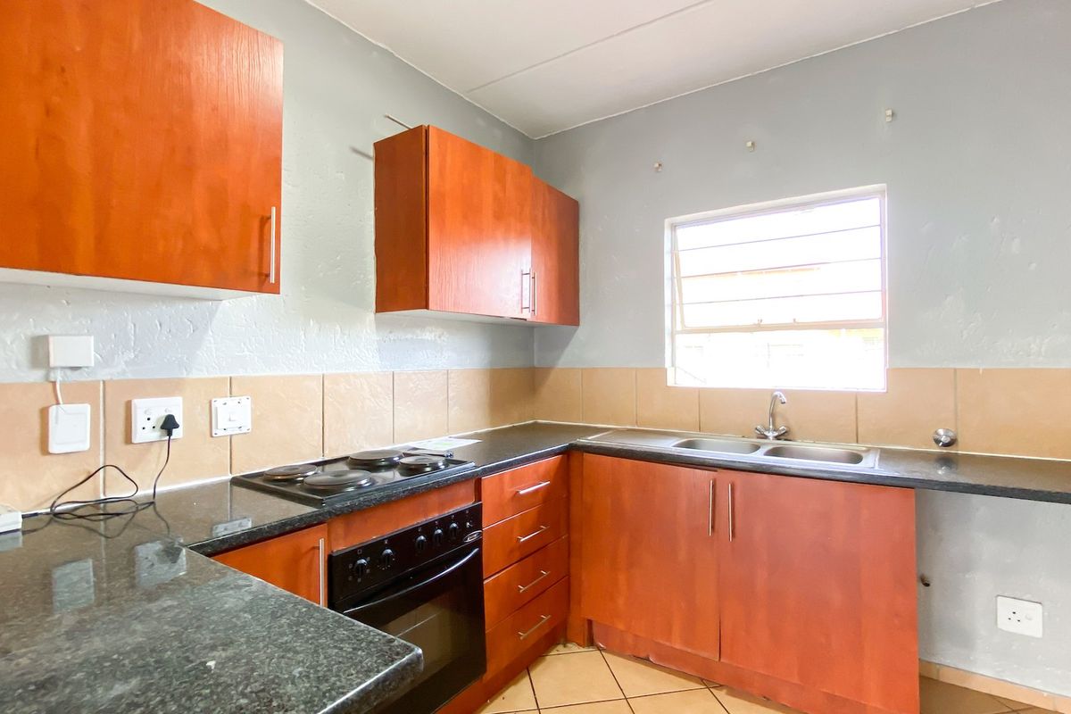 A functional kitchen featuring wood-finish cabinetry, dark laminate countertops, a built-in electric oven and hob, and a double sink with a tiled backsplash.
