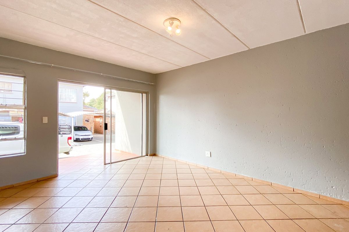 An empty living room featuring tiled flooring, a sliding glass door leading to the exterior, and a large window providing natural light.