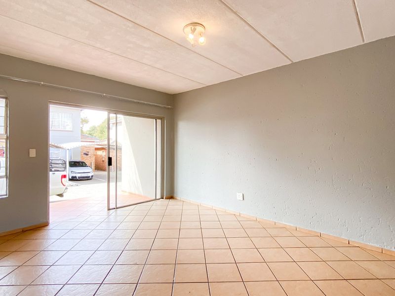 An empty living room featuring tiled flooring, a sliding glass door leading to the exterior, and a large window providing natural light.