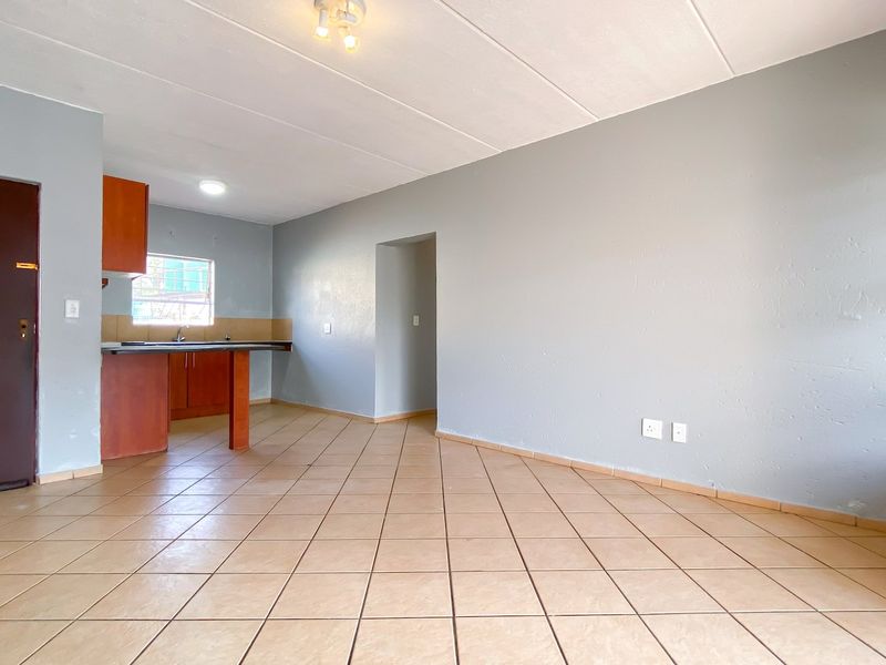 An open-plan living and kitchen area featuring tiled flooring, neutral wall tones, and functional kitchen cabinetry with a built-in sink.