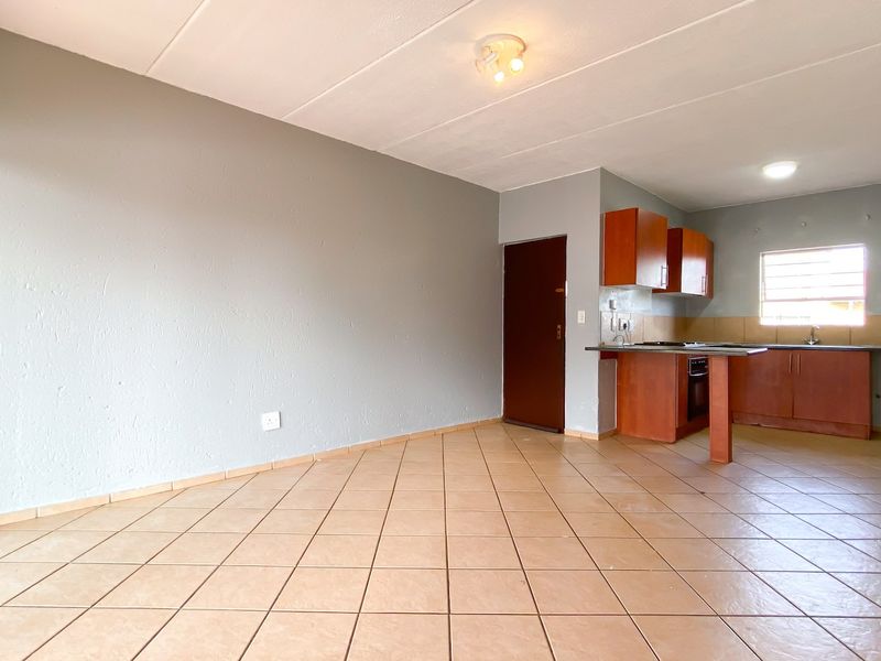 An open-plan living and kitchen area featuring tiled flooring, built-in wooden cabinetry, and a functional kitchen layout.