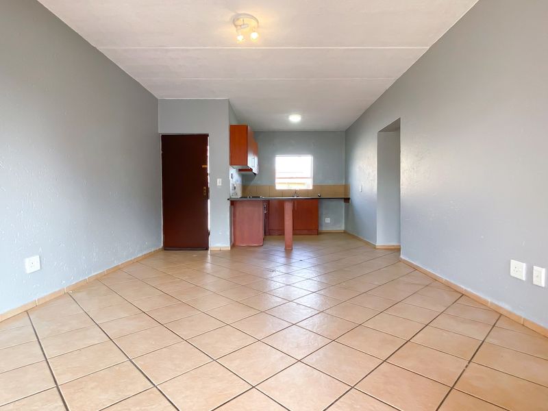 An open-plan living and kitchen area featuring tiled flooring, neutral wall paint, and functional built-in kitchen cabinetry.