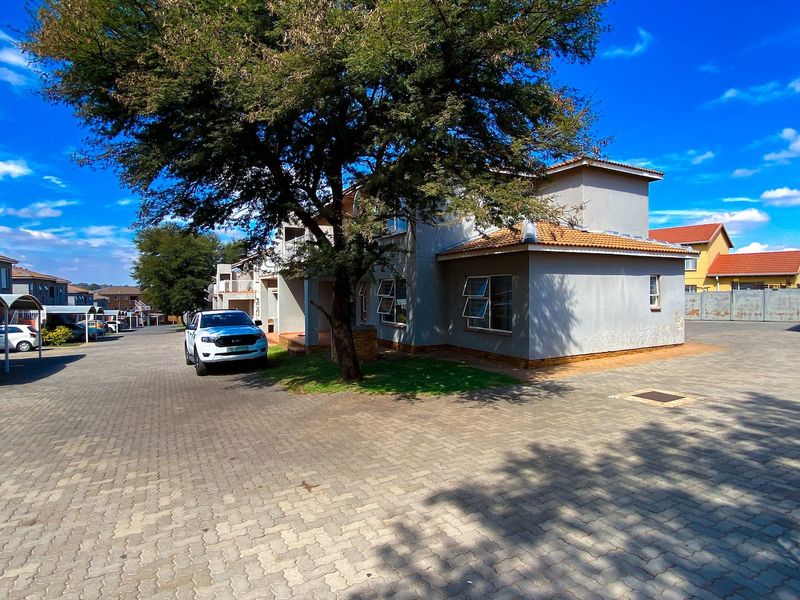 Exterior view of an apartment complex featuring a paved driveway, covered parking carports, and a residential building with a tiled roof.