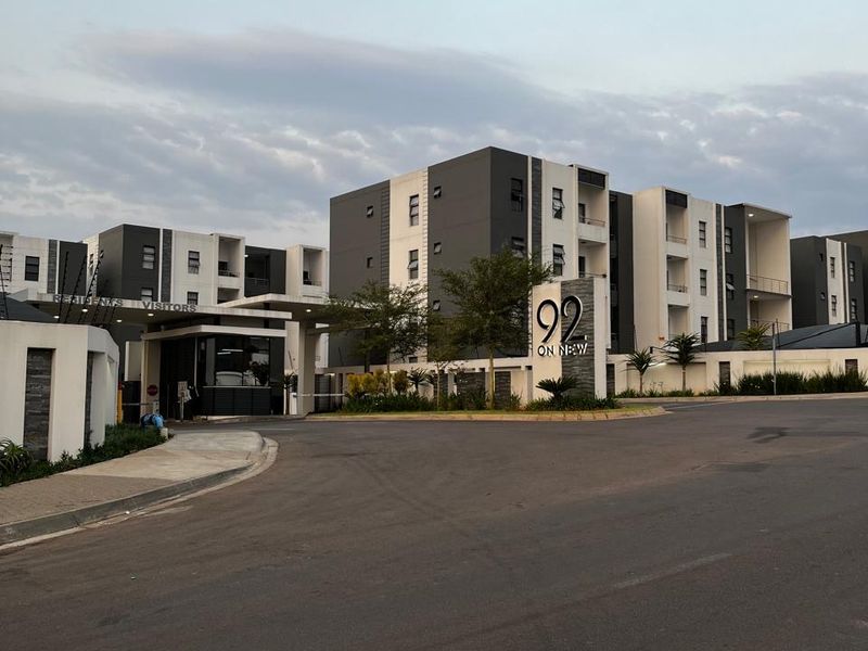 Exterior view of the modern apartment complex entrance, featuring a security gatehouse, paved driveway, and clear signage for 92 on New.