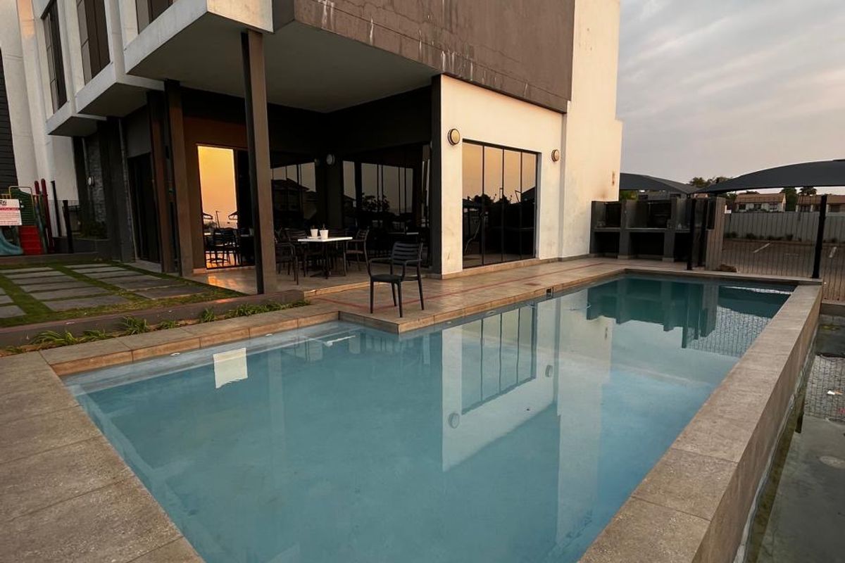 Modern apartment exterior featuring a private swimming pool, paved patio area, and a built-in outdoor braai facility.